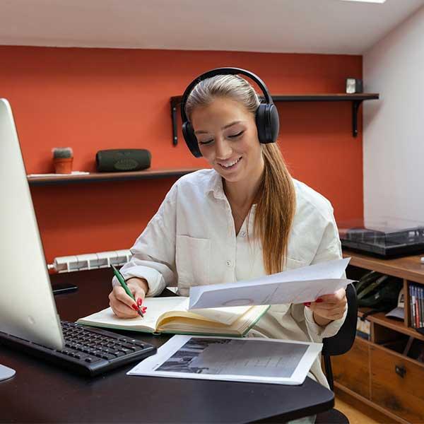 Woman wearing headphones making notes while working at home