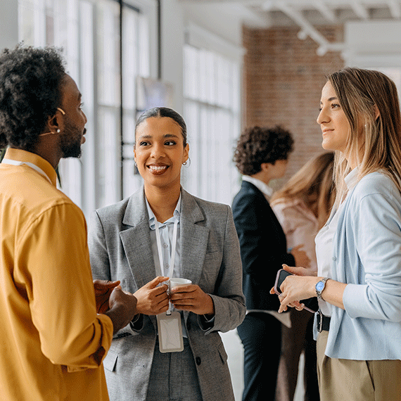 Three business professionals having a conversation in a bright modern office with brick walls and large windows.