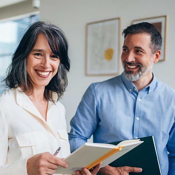 Smiling woman in white shirt and man in blue shirt reviewing documents together in a bright office with framed art.